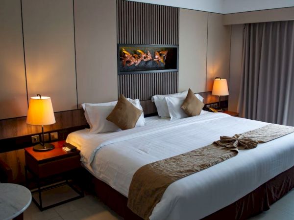 A neatly arranged hotel room with a queen-sized bed, pillows, bedside tables with lamps, and a modern decor theme.