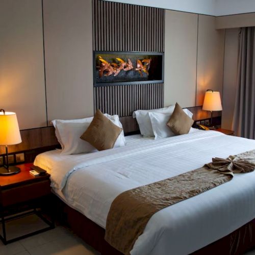 A neatly made hotel bed with accent pillows, bedside lamps, and artwork above it; the room looks cozy and inviting.
