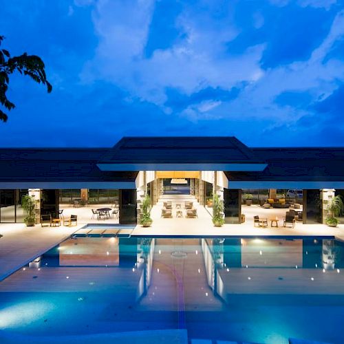 A luxurious building with a lit swimming pool at night, surrounded by modern architecture and ambient lighting.