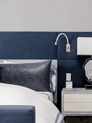 A modern bedroom with a blue headboard, white bed, pillows, and a nightstand with a lamp and decor.