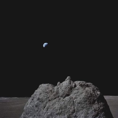 Lunar surface with a prominent rock in the foreground and Earth visible in the dark sky above.