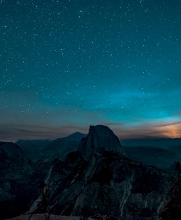 A starry night sky above a mountain landscape with a glowing horizon, creating a serene and captivating natural scene.