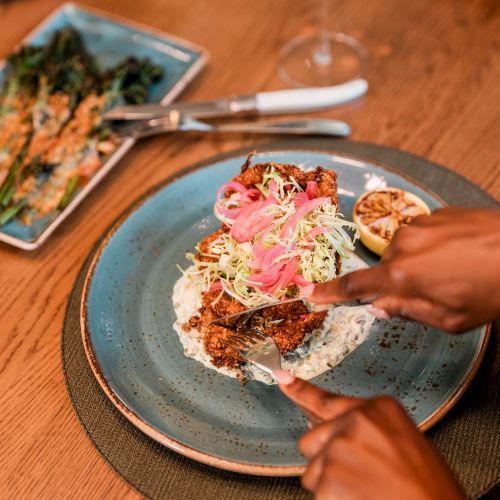 A person is preparing or eating vibrant tacos or flatbreads topped with veggies and sauce, with hands arranging toppings on a blue plate.
