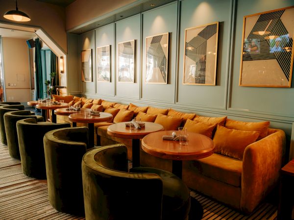 A stylish, modern lounge with green chairs, mustard sofas, wooden tables, and geometric artwork on blue walls.