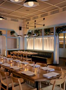 A rustic dining area with long wooden tables, hanging lights, and a warm, inviting cafe or restaurant atmosphere.