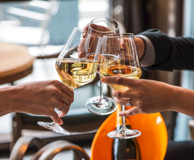 Three people clinking glasses of white wine in a celebratory toast, with a blurred background suggesting a casual setting.