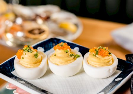 The image shows a plate of three deviled eggs garnished with seasoning and herbs, served on a blue and white dish.