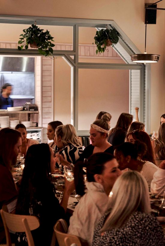 A busy restaurant with people dining and a visible kitchen in the background, creating a lively and warm atmosphere.