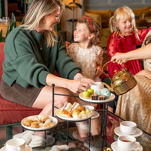 A group of people enjoys tea with snacks, including pastries and fruits, elegantly arranged on a tiered tray.