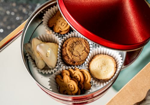 A red tin contains assorted cookies, including a heart-shaped one and animal-shaped ones, arranged in paper cups.