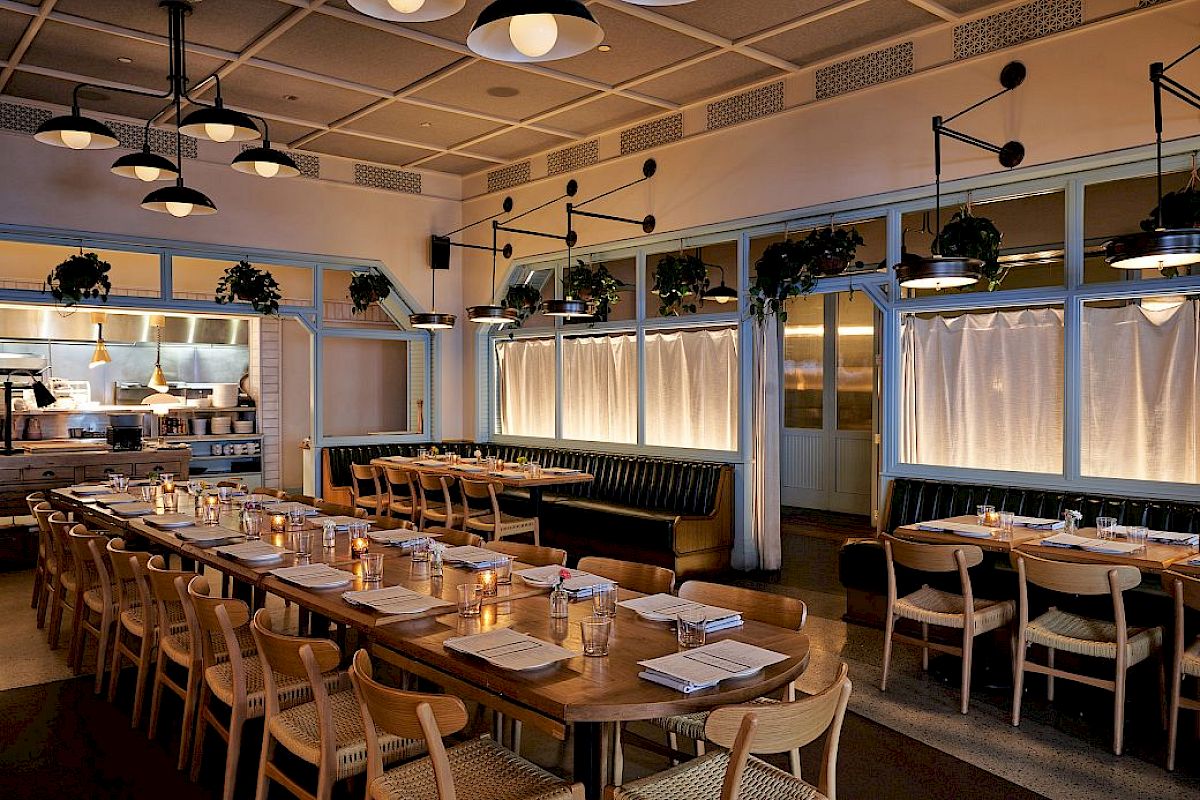 This image shows a cozy restaurant interior with wooden tables, chairs, pendant lights, and candles, creating a warm and inviting atmosphere.