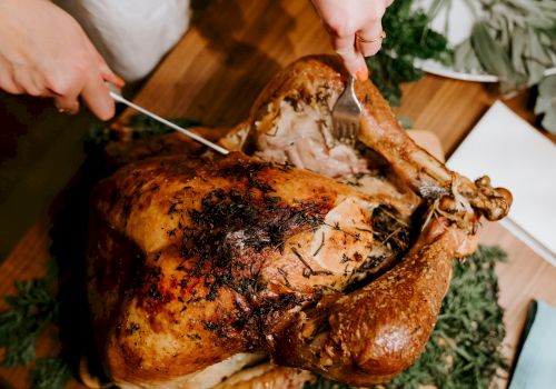 Outdoor cooking: people carving a roasted, herb-crusted meat with tongs and a carving fork.