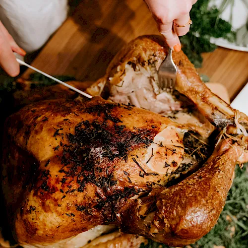 Outdoor cooking: people carving a roasted, herb-crusted meat with tongs and a carving fork.