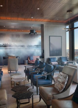 The image shows a stylish lounge with comfortable seating, large windows offering a scenic view, and a modern design aesthetic.