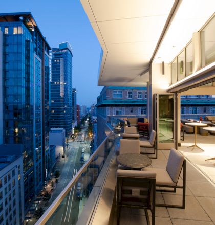 A modern balcony view of a cityscape at dusk, featuring high-rise buildings and well-lit seating areas along the terrace.