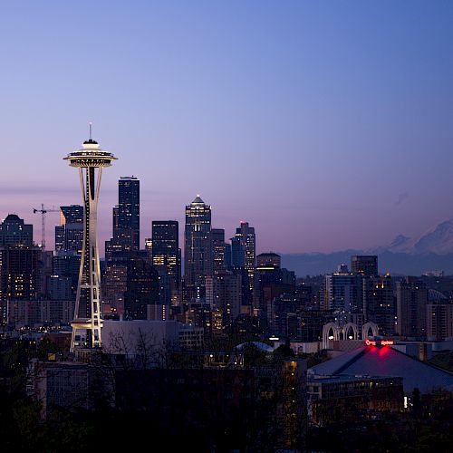 The image shows the Seattle skyline at dusk, featuring the iconic Space Needle and Mount Rainier in the background.